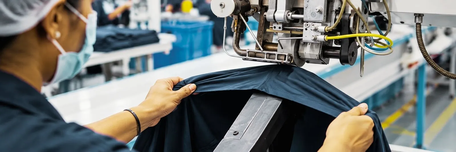 A garment worker guiding a dark garment through an automatic sewing machine